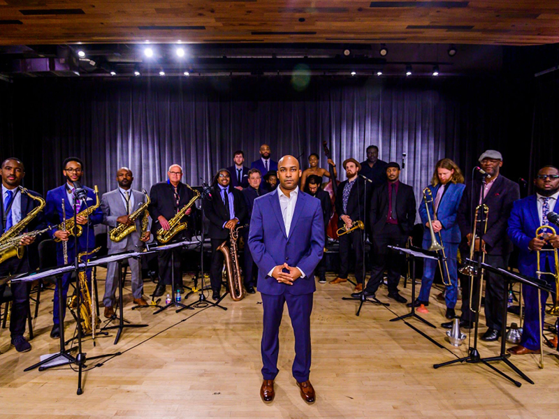 Man standing on stage with jazz orchestra behind him.