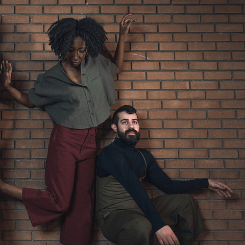 Two people resting against a brick wall